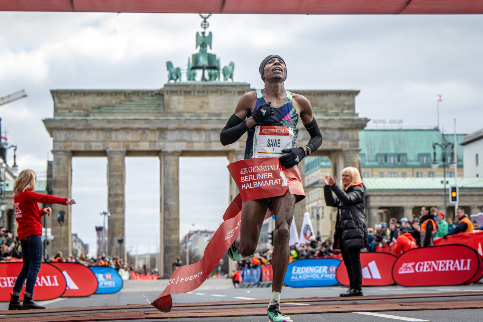 A runner crosses the finish line in first place with arms raised in victory, capturing the success of a well-structured weekly training plan.