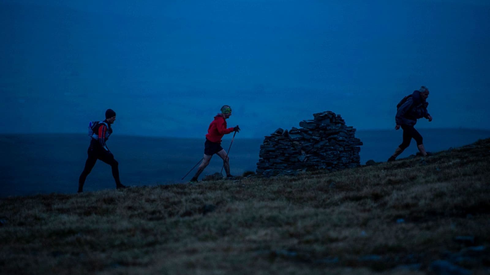 Triathlete running over rocky and uneven trail terrain at night while maintaining careful footing under headlamp illumination.