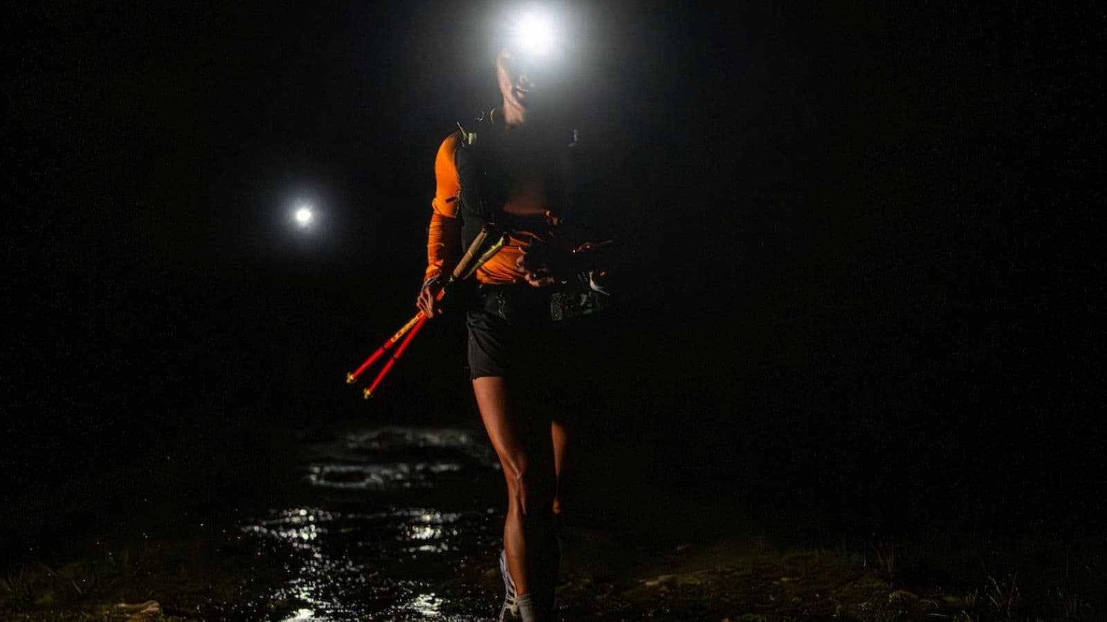 Triathlete wearing a bright headlamp while running on a forest trail after sunset during night trail running training.
