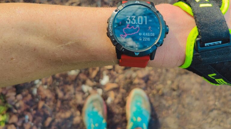 Trail runner checking a GPS sports watch before starting a run through a forest trail.