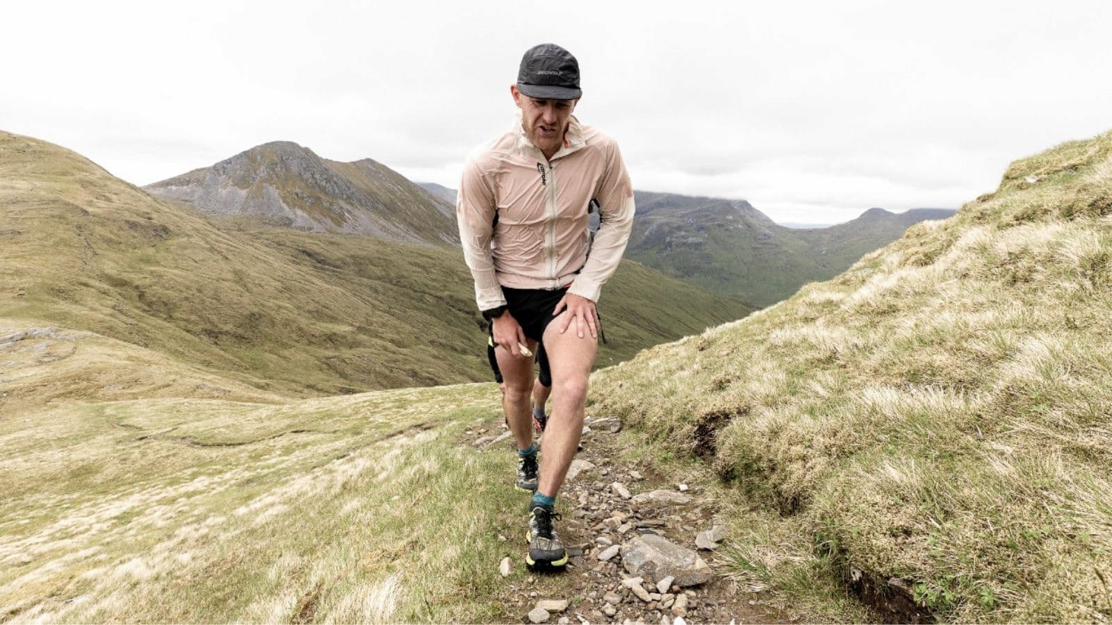 Trail runner stopping on a forest trail after experiencing sudden leg pain during a training run.