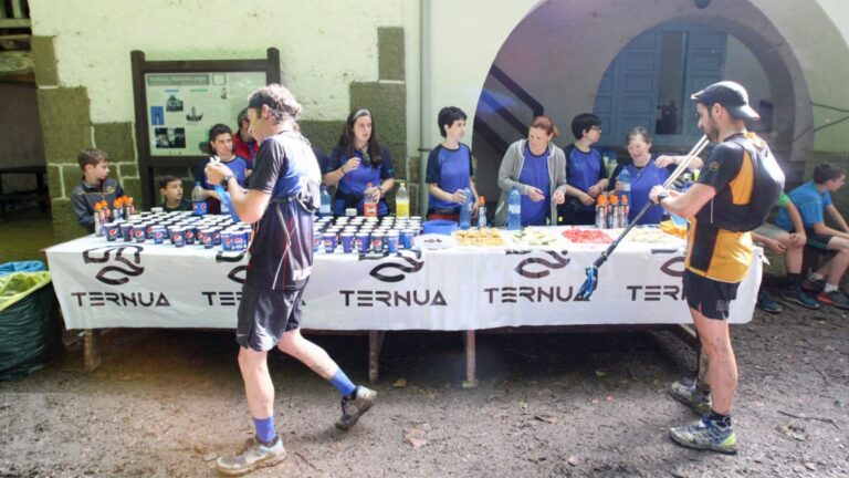 Trail runner approaching an aid station during a long-distance trail race while preparing to refill hydration and collect nutrition.