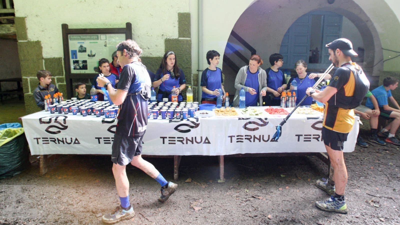 Trail runner approaching an aid station during a long-distance trail race while preparing to refill hydration and collect nutrition.