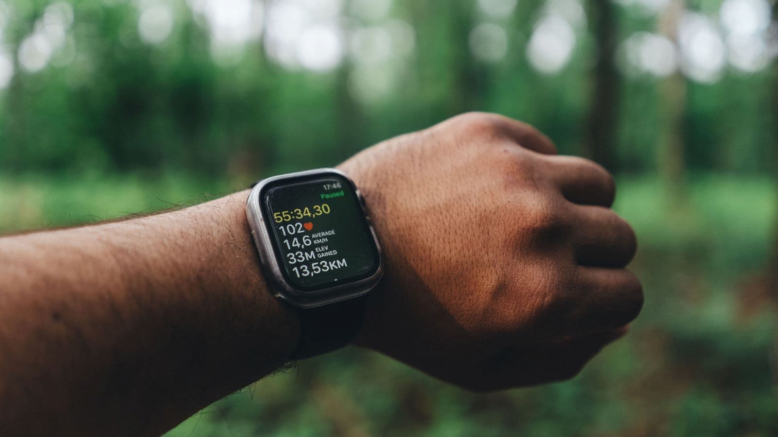 Trail runner checking GPS data on a sports watch while running along a remote mountain trail.