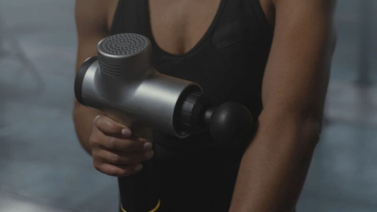 Runner using a massage gun on the shoulder and upper arm muscles after completing a long-distance running race.