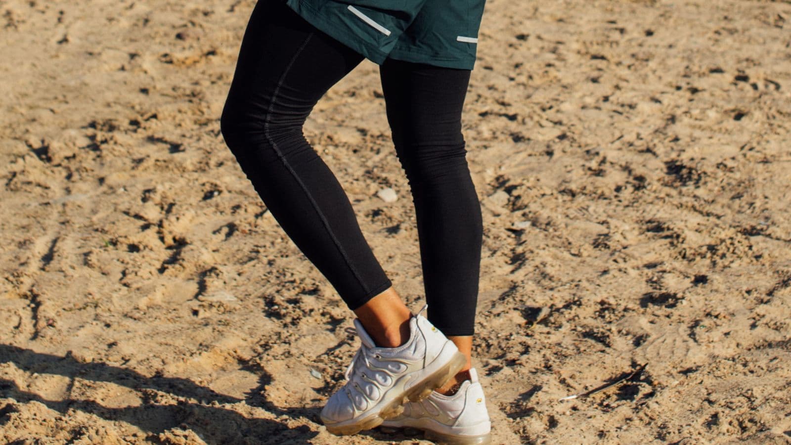 Trail runner wearing compression tights while running on a rocky mountain trail during an endurance training session.