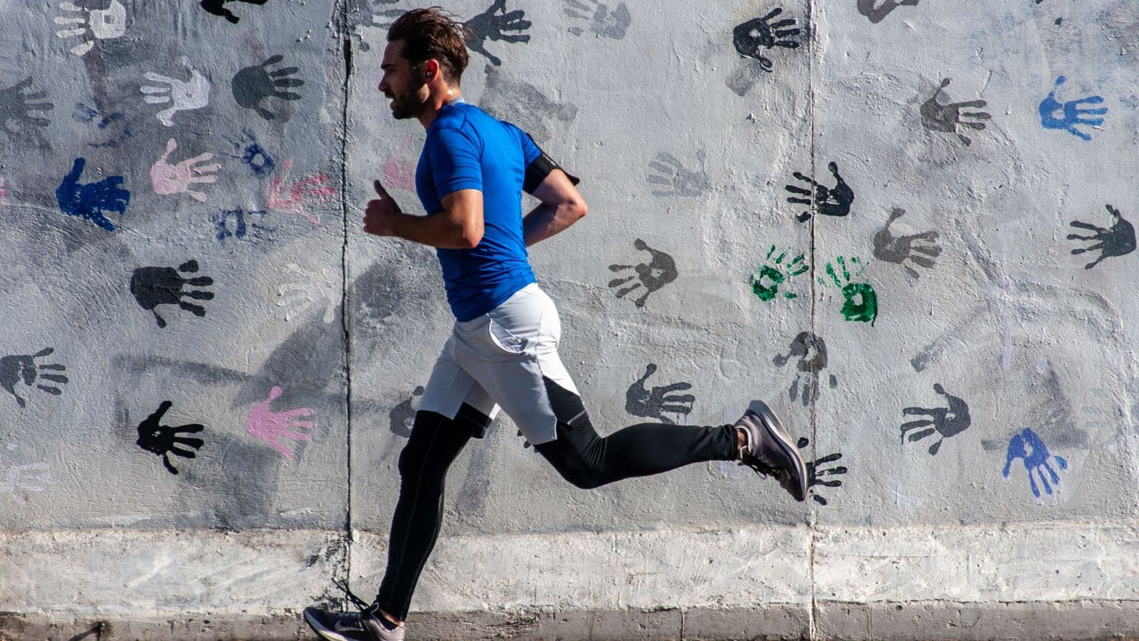 Trail runner wearing compression tights while climbing a steep forest trail during a long-distance training run.