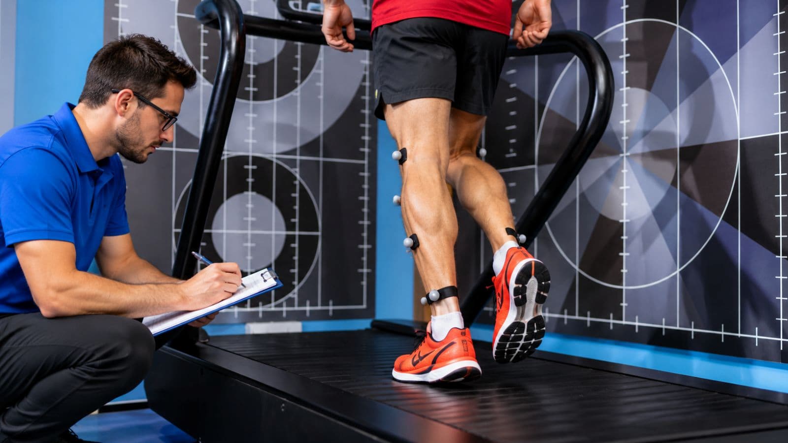 Runner undergoing treadmill gait analysis while a specialist records running form and movement patterns using a video camera.