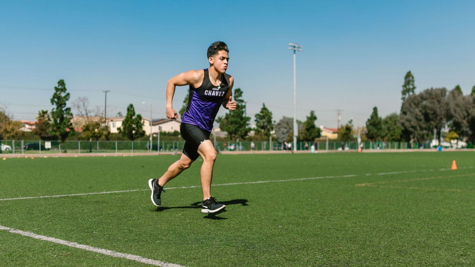 Distance runner maintaining a controlled, challenging pace during a critical velocity interval workout on an outdoor athletics track.