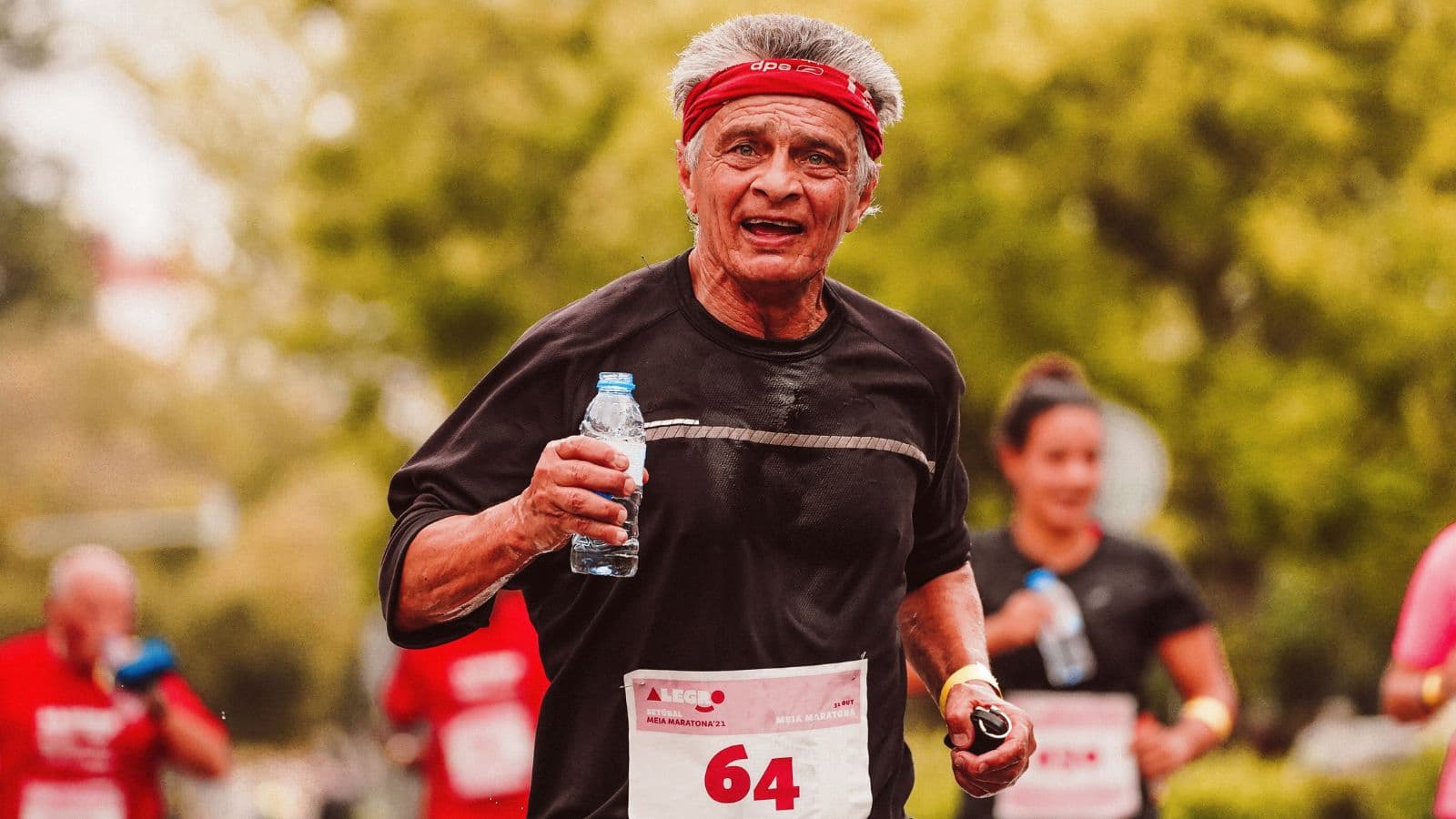 Older ultrarunner maintaining a steady pace during a long-distance trail race through mountainous terrain.